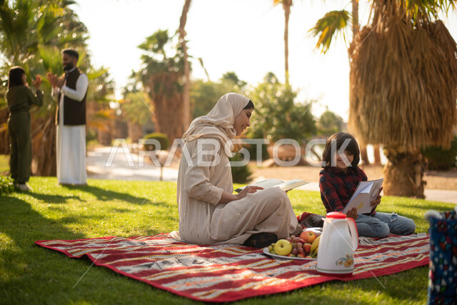 امرأة عربية خليجية سعودية برفقة ولدها  في إحدى الحدائق العامة بالسعودية ، ممارسة هواية الرسم والكتابة ، نزهه في الهواء الطلق ، عطلة صيفية، الجلوس في الطبيعة الخضراء.