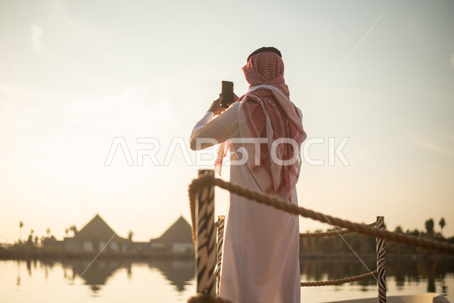 رجل عربي خليجي سعودي التقاط صور تذكارية باستخدام الهاتف المحمول ، نزهة في الهواء الطلق ،  قضاء اوقات ممتعة في احد الاماكن السياحية ، بحيرة مائية ، نزهات ترفيهية في المملكة العربية السعودية.