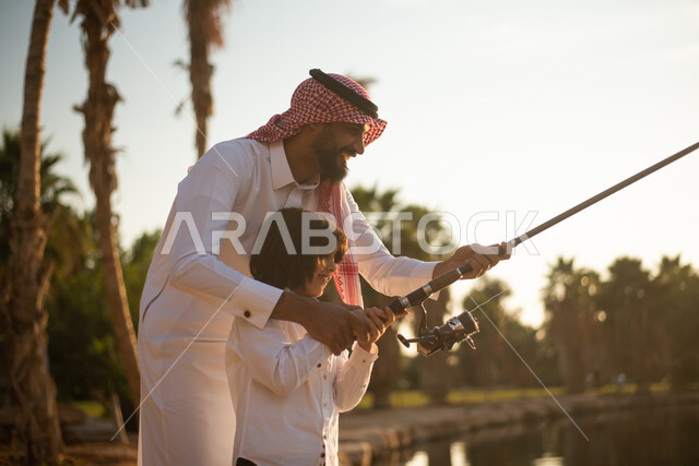 رجل سعودي  خليجي  عربي يعلم ولده  صيد الاسماك ، ممارسة الأنشطة الترفيهية في الهواء الطلق ،  رحلة صيد الأسماك ، عطلة صيفية ، حدائق ونزهات ترفيهية في المملكة العربية السعودية.
