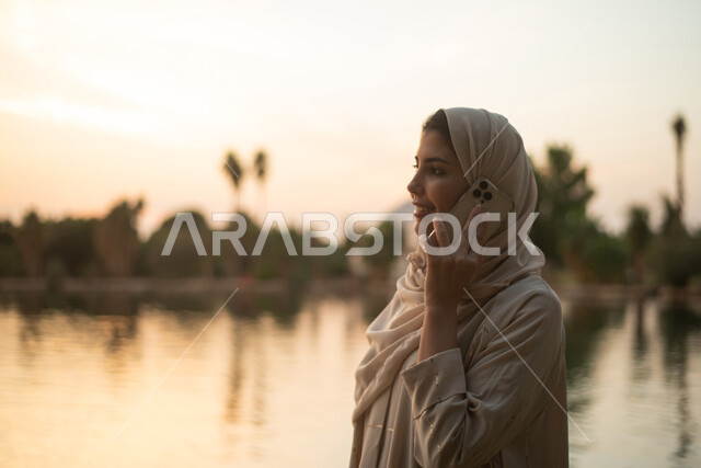 A close-up of a Saudi Gulf Arab woman making a voice call using a mobile phone, a recreational resort, theme parks and gardens, public parks in the Kingdom of Saudi Arabia.
