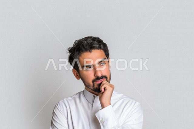 بورتريه لرجل عربي سعودي خليجي باللباس التقليدي , يقوم بإيماءات وجه ويدين تدل على التفكير و التركيز ، اشارات يدين تدل على الحيرة , خلفية بيضاء .