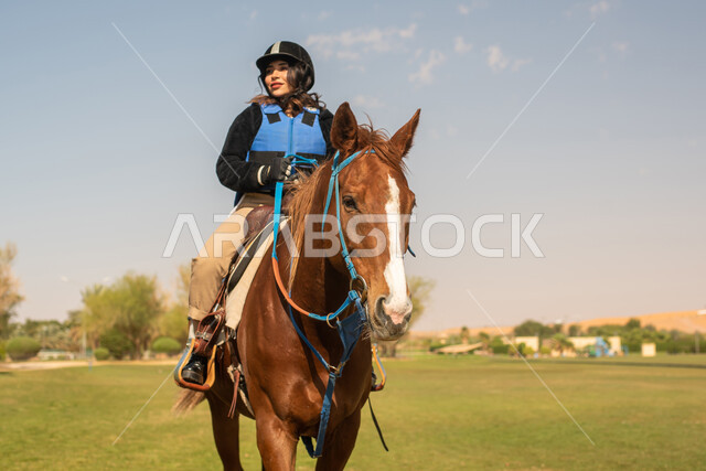 فتاة عربية سعودية خليجية تمتطي خيل عربي أصيل وترتدي زي الفروسية, تربية الخيول في الاسطبل، هواية ركوب الخيل, حصان بني، مزرعة تدريب وترويض الخيول في السعودية ، نادي الفروسية ،انشطة ترفيهية 