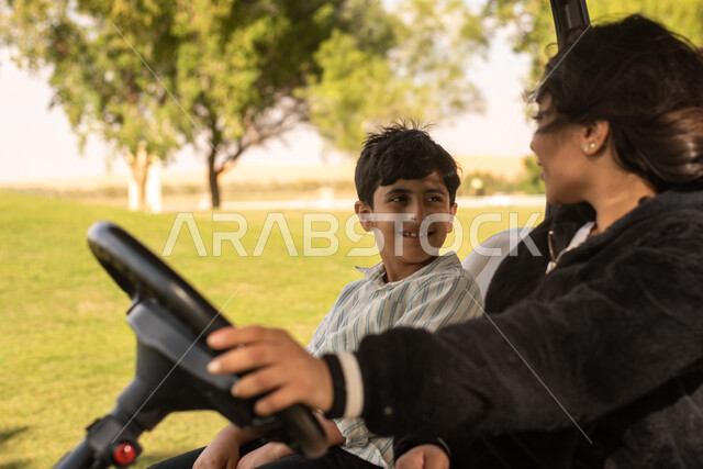 Summer vacation, close-up of a Saudi Arab Gulf woman with her son inside an electric golf car to transport passengers, spending quality time with children, family leisure activities, golf course, golf club in the Kingdom of Saudi Arabia, sports activities