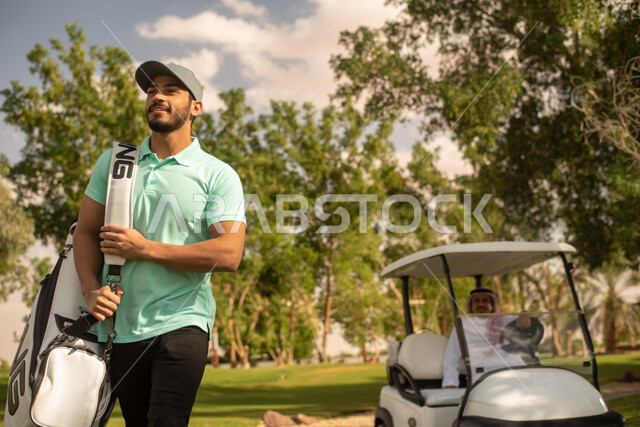 شابان عربيان خليجيان سعوديان في ملعب الجولف، سيارة جولف كهربائية لنقل الركاب، ممارسة لعبة الغولف، مساحات واسعة خضراء، أنشطة رياضية، رياضة لعبة الجولف، الألعاب الأولمبية الصيفية، أنشطة ترفيهية ممتعة , خلفية الطبيعة الخضراء .