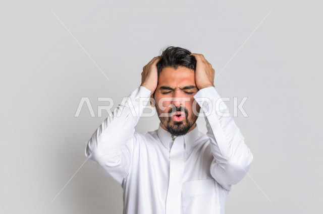بورتريه لرجل عربي سعودي خليجي باللباس التقليدي , يقوم بإيماءات وجه ويدين تدل على الشعور بالصداع, ألم بالرأس, الإحساس بالمرض, التعب والإرهاق, الحاجه للعلاج, طلب المساعده , خلفية بيضاء .