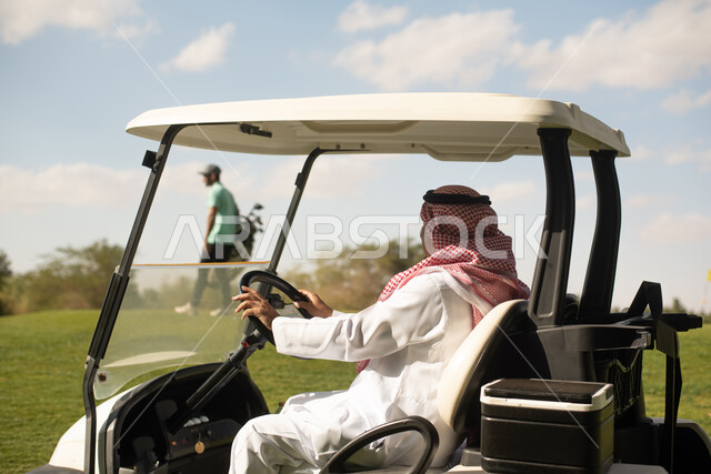صورة من الخلف لرجلان عربيان خليجيان سعوديان,  سيارة جولف كهربائية لنقل الركاب، ممارسة لعبة الغولف على مساحات واسعة خضراء، أنشطة رياضية في السعودية، رياضة لعبة الجولف، الألعاب الأولمبية الصيفية، أنشطة ترفيهية ممتعة، ملعب الجولف