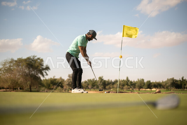 رجل عربي خليجي سعودي يرتدي الزي الكاجوال , ملعب الجولف, ممارسة لعبة الغولف، مساحات خضراء واسعة، أنشطة رياضية في السعودية، رياضة لعبة الجولف، الألعاب الأولمبية الصيفية، أنشطة ترفيهية ممتعة، الإستمتاع باللعب