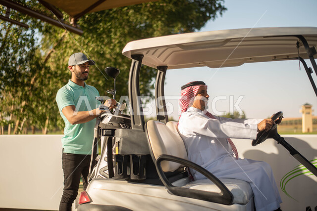 Summer Olympics sports, two Saudi Arabian Gulf men on the golf course, summer, recreational sports activities in Saudi Arabia, electric golf car to transport passengers, golf practice on large green areas, golf game, green nature background.