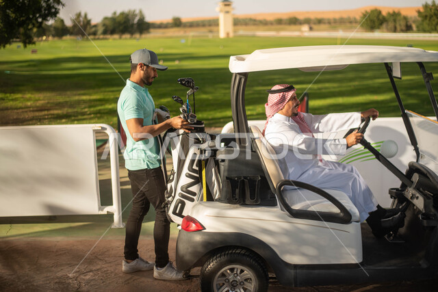 سيارة جولف كهربائية لنقل الركاب, رجلان عربيان خليجيان سعوديان في ملعب الجولف، ممارسة لعبة الغولف على مساحات واسعة خضراء, لعبة الجولف، رياضات الألعاب الأولمبية الصيفية، أنشطة رياضية  ترفيهية في السعودية, خلفية الطبيعة الخضراء.
