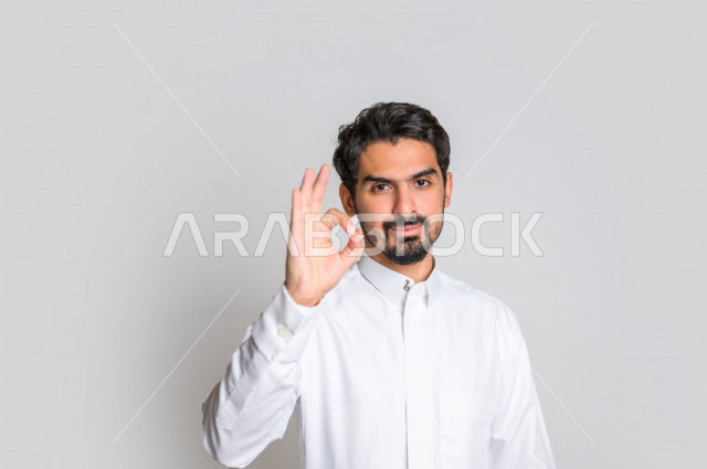 بورتريه لرجل عربي سعودي خليجي  باللباس التقليدي , يقوم بإيماءات وجه تدل على الرضى ، إشارات يدين تدل على الموافقة والإعجاب ، علامة الجودة , الإمتياز والتميز , القبول والموافقة , خلفية بيضاء .