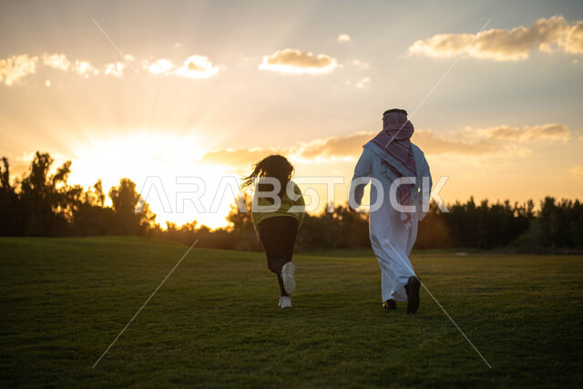 صورة من الخلف لرجل عربي  خليجي سعودي يقضي اوقات ممتعة مع ابنته في إحدى الحدائق العامة, عطلة صيفية، نزهه في الهواء الطلق، جولة في الطبيعة الخضراء، مزارع واستراحات، أنشطة ترفيهية عائلية