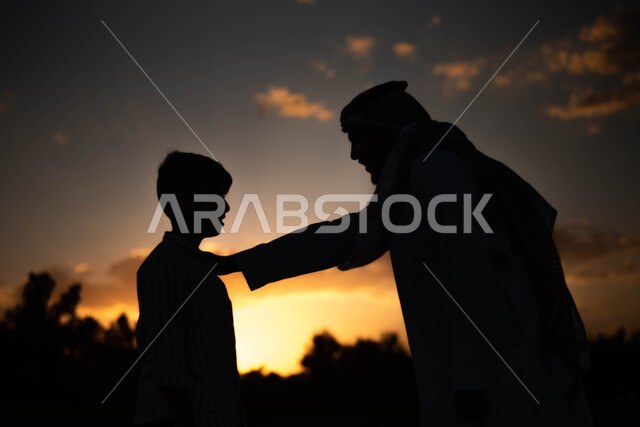 صورة ظلية لرجل عربي خليجي سعودي مع ابنه في الخارج  , قضاء أوقات ممتعة مع الأبناء, دردشة ومحادثات, منظر غروب الشمس في السماء , أنشطة ترفيهية في الهواء الطلق ,خلفية الطبيعة, سيلوليت .