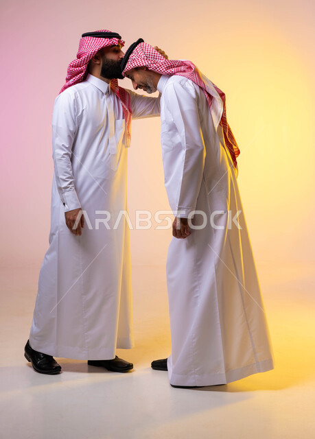 بورتريه لرجل عربي خليجي سعودي يقوم بتقبيل رأس والده ، صورة الجسم بالطول الكامل ، بر الوالدين وصلة الارحام ،  ايماءات تدل على التقدير والاحترام ، ارتداء الزي التقليدي السعودي ،التجمعات الأسرية ،  التهنئه بالعيد السعيد ، خلفية ملونة
