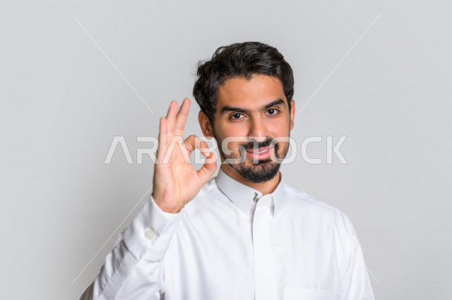 بورتريه لرجل عربي سعودي خليجي  باللباس التقليدي , يقوم بإيماءات وجه تدل على الرضى ، إشارات يدين تدل على الموافقة والإعجاب ، علامة الجودة , الإمتياز والتميز , القبول والموافقة , خلفية بيضاء .