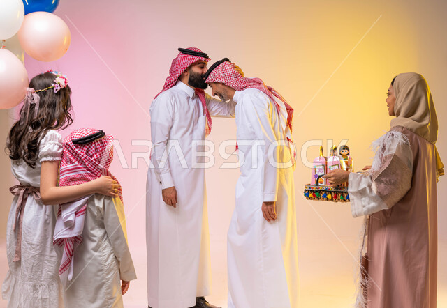 اجواء عائليه سعيده  ، رجل عربي خليجي سعودي يقوم بتقبيل رأس والده ، بورتريه لعائلة عربيه سعوديه خليجيه في غرفة المعيشة  تحتفل بأيام العيد ، تقديم توزريعات وقرقيعان العيد  ، عيد سعيد ، الاحتفال بالأعياد الإسلامية  ، خلفية ملونة