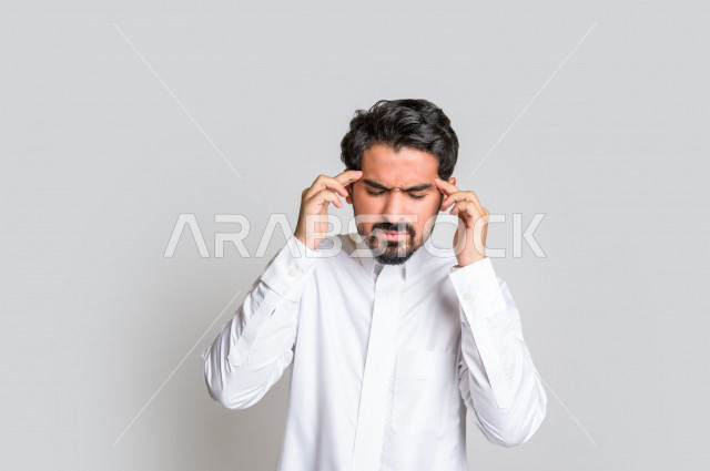Portrait of a Saudi Arabian Gulf man in traditional dress, facial and hands gestures indicating headache, headache, feeling sick, fatigue and exhaustion, needing treatment, asking for help, white background.