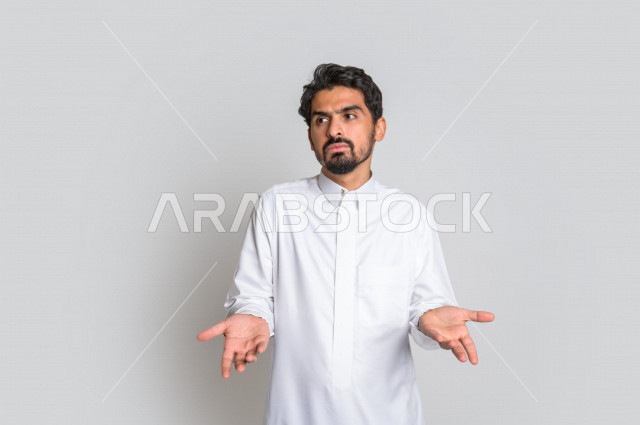 بورتريه لرجل عربي سعودي خليجي باللباس التقليدي , يقوم بإيماءات وجه ويدين تدل على التساؤل والإستغراب , الإستفهام عن شيء ما , عدم المعرفة ,خلفية بيضاء .