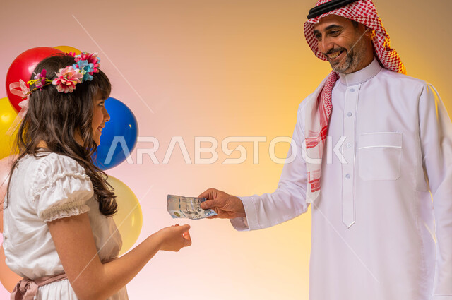 بورتريه لرجل عربي سعودي خليجي يرتدي الزي السعودي الخليجي يقوم بتقديم العيدية لفتاة عربية خليجية سعودية ، إيماءات تدل على الفرح والسرور بالعيد السعيد , مناسبات واعياد اسلاميه ، بالونات وزينة العيد ، خلفية ملونة