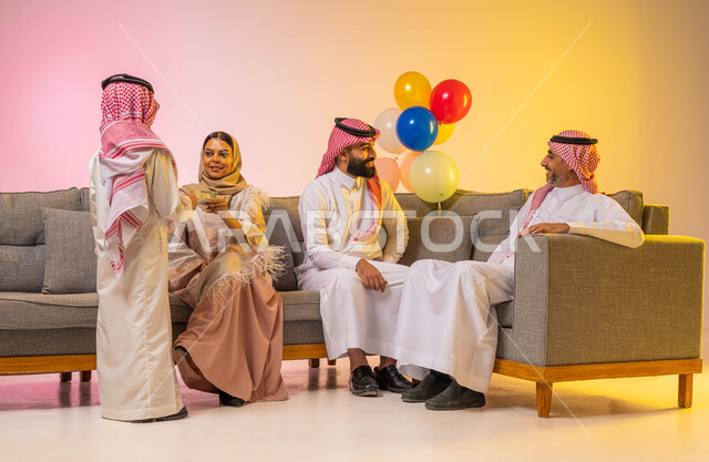 بورتريه لعائلة عربية خليجية سعودية وأمراه عربيه سعوديه خليجيه تقوم بتقديم العيديات للأطفال ، أجواء عائليه سعيده ، إيماءات تدل على الفرح والسرور بالعيد السعيد, الزيارات والتجمعات الاسريه, مناسبات واعياد اسلاميه ، خلفية ملونة