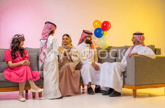 تقديم العيديات للأطفال ، أجواء عائليه سعيده ، بورتريه لعائلة عربية خليجية سعودية تحتفل بقدوم العيد في غرفة الجلوس  , ايماءات تدل على الفرح والسرور بالعيد السعيد, الزيارات والتجمعات الاسريه, مناسبات واعياد اسلاميه ، خلفية ملونة