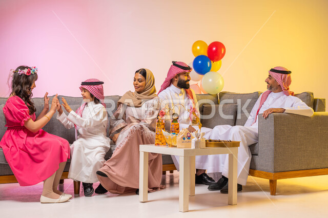بورتريه لعائلة عربية خليجية سعودية   تحتفل بقدوم العيد السعيد في غرفة الجلوس ، إيماءات وجه تدل على الفرح والسعادة ، الزيارات والتجمعات الاسريه, مناسبات واعياد اسلاميه ، أجواء عائليه سعيده ، المرح واللعب في العيد ، خلفية ملونة