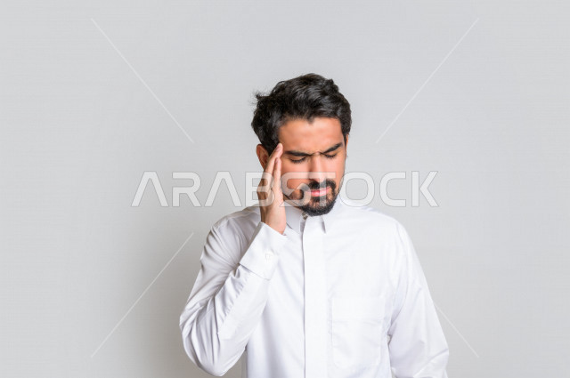 بورتريه لرجل عربي سعودي خليجي باللباس التقليدي , يقوم بإيماءات وجه ويدين تدل على الشعور بالصداع, ألم بالرأس, الإحساس بالمرض, التعب والإرهاق, الحاجه للعلاج, طلب المساعده , خلفية بيضاء .
