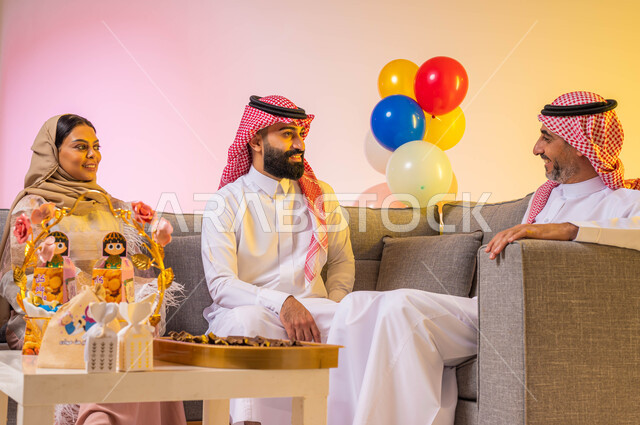 أجواء العيد في السعودية ، بورتريه لعائلة عربية خليجية سعودية تحتفل بقدوم العيد المبارك في غرفة المعيشة ، الاحتفال بالعيد السعيد ، إيماءات وجه تدل على الفرح والسعادة ، بالونات وزينة العيد ، خلفية ملونة