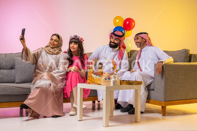 زيارات وتجمعات عائليه ، بورتريه لعائلة عربية سعودية تحتفل بقدوم العيد السعيد ، التقاط صورة سيلفي عن طريق استخدام الهاتف المحمول ، الاحتفال بالعيد السعيد ، إيماءات وجه تدل على الفرح والسعادة ، خلفية ملونة