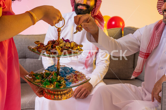 بورتريه لفتاة عربية خليجية سعودية  تقدم حلوى العيد للضيوف, مناسبات واعياد اسلاميه, زيارات وتجمعات عائليه, اكرام الضيف وحسن الاستقبال ، خلفية ملونة