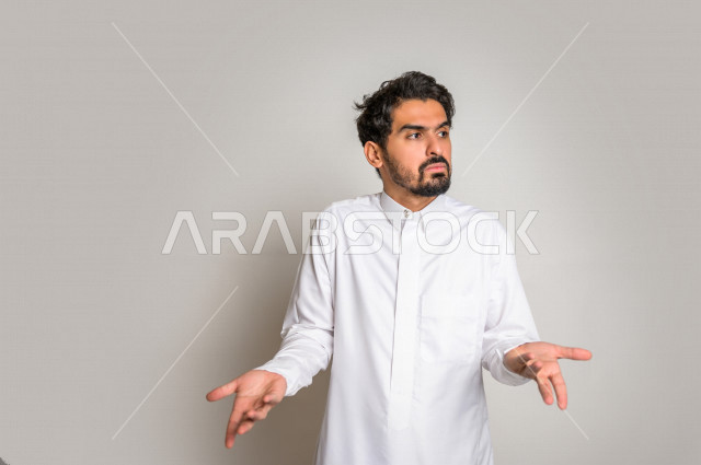 بورتريه لرجل عربي سعودي خليجي باللباس التقليدي , يقوم بإيماءات وجه ويدين تدل على التساؤل والإستغراب , الإستفهام عن شيء ما , عدم المعرفة ,خلفية بيضاء .