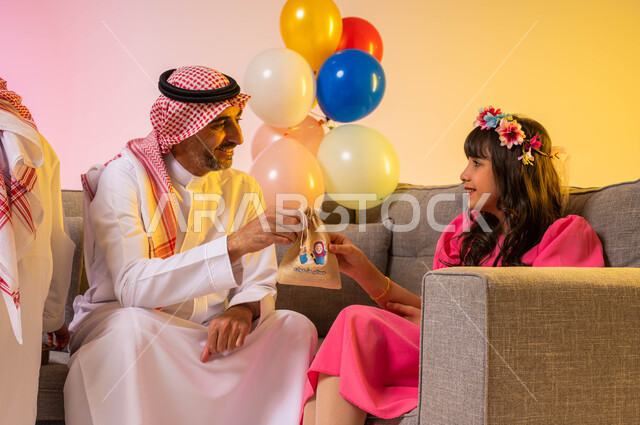 بورتريه لأب عربي خليجي سعودي يقدم لابنته توزريعات وقرقيعان العيد ، ارتداء اللباس السعودي التقليدي ، التهنئة بقدوم العيد ، أجواء العيد في المملكة العربية السعودية  ، خلفية ملونة