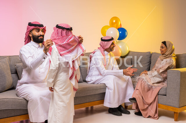 A happy family atmosphere, a portrait of a Saudi Arabian Gulf father wearing the traditional Saudi dress, helping his son to wear Eid clothes, preparing for the happy Eid, Islamic holidays and occasions, colorful background