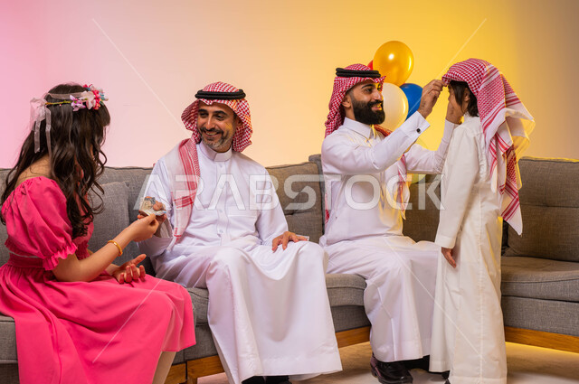 بورتريه لعائله عربيه سعوديه خليجيه سعيده في غرفة الجلوس , إرتداء اللباس السعودي التقليدي في الأعياد والمناسبات, تقديم العيديات للأطفال, ايماءات تدل على الفرح والسرور بالعيد السعيد, الزيارات والتجمعات الاسريه, مناسبات واعياد اسلاميه ، خلفية ملونة