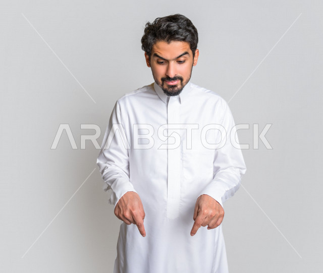 بورتريه لرجل عربي سعودي خليجي يرتدي الثوب السعودي, يؤشر بيديه للأسفل الى شيء ما , حركات تدل على المكان , خلفية بيضاء .