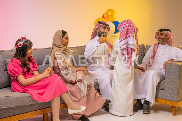 بورتريه لعائله عربيه سعوديه خليجيه في غرفة الجلوس تحتفل بالعيد السعيد ، ولد سعودي يقوم بتبخير وتعطير الضيوف، بالونات وزينة العيد، مناسبات  واعياد اسلاميه، خلفيه ملونه