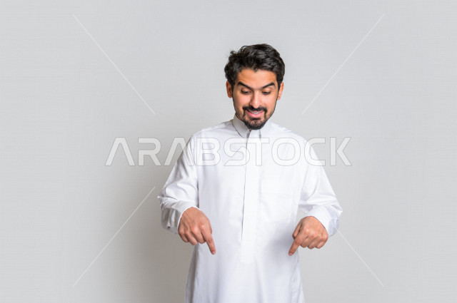 بورتريه لرجل عربي سعودي خليجي يرتدي الثوب السعودي, يؤشر بيديه للأسفل الى شيء ما , حركات تدل على المكان , خلفية بيضاء .
