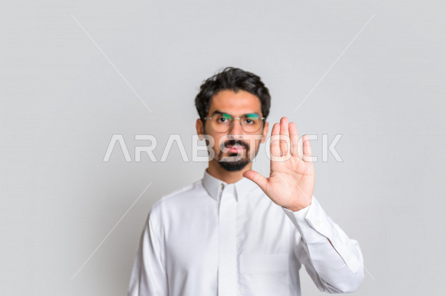بورتريه لرجل عربي سعودي خليجي يرتدي الثوب السعودي, إيماءات يدين تدل على الأمر بالتوقف عن فعل شيء ما, الشعور بالخوف و الإنزعاج, الرفض والإمتناع , خلفية بيضاء .