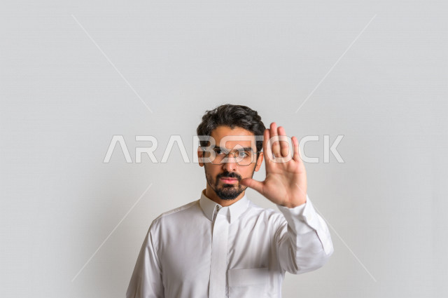 بورتريه لرجل عربي سعودي خليجي يرتدي الثوب السعودي, إيماءات يدين تدل على الأمر بالتوقف عن فعل شيء ما, الشعور بالخوف و الإنزعاج, الرفض والإمتناع , خلفية بيضاء .
