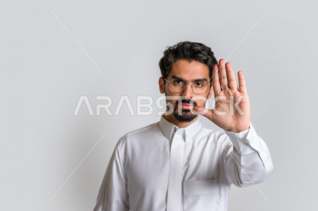 بورتريه لرجل عربي سعودي خليجي يرتدي الثوب السعودي, إيماءات يدين تدل على الأمر بالتوقف عن فعل شيء ما, الشعور بالخوف و الإنزعاج, الرفض والإمتناع , خلفية بيضاء .