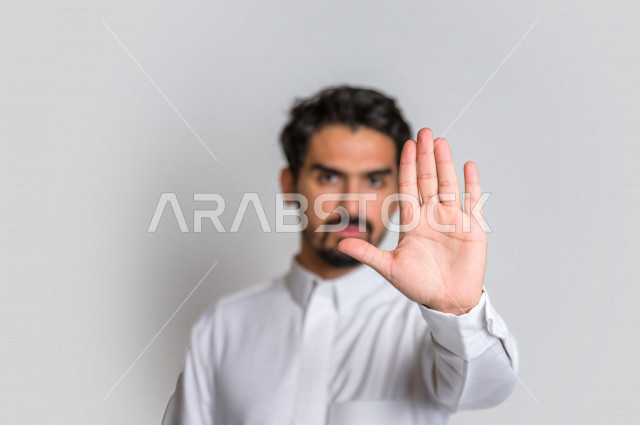 بورتريه لرجل عربي سعودي خليجي يرتدي الثوب السعودي, إيماءات يدين تدل على الأمر بالتوقف عن فعل شيء ما, الشعور بالخوف و الإنزعاج, الرفض والإمتناع , خلفية بيضاء .