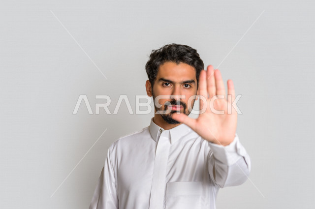 Portrait of a Saudi Arabian Gulf man wearing the Saudi dress, hand gestures indicating the order to stop doing something, feeling fear and annoyance, rejection and abstinence, white background.
