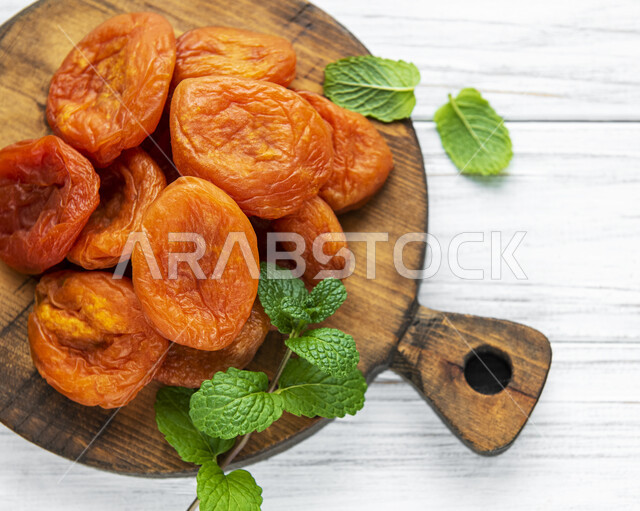 مشمش مجفف على طبق خشبي, نوع من أنواع الفواكه المجففة , المشمش المجفف , فواكه مجففة صحية ولذيذة , عنصر غذائي مفيد للصحة, خلفية بيضاء