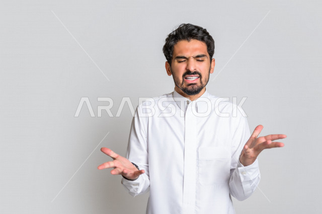 بورتريه لرجل عربي سعودي خليجي باللباس التقليدي , يقوم بإيماءات وجه ويدين تدل على الصراخ والتشاؤوم , التساؤل والإستغراب , الإستفهام عن شيء ما , خلفية بيضاء .