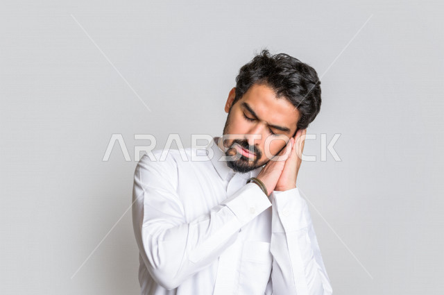بورتريه لرجل عربي سعودي خليجي يرتدي الثوب السعودي, إيماءات وجه ويدين تدل على النعاس , الشعور بالتعب , الحاجه الى النوم والراحه, الإحساس بالإرهاق, الكسل والخمول , النوم بعمق , خلفية بيضاء .