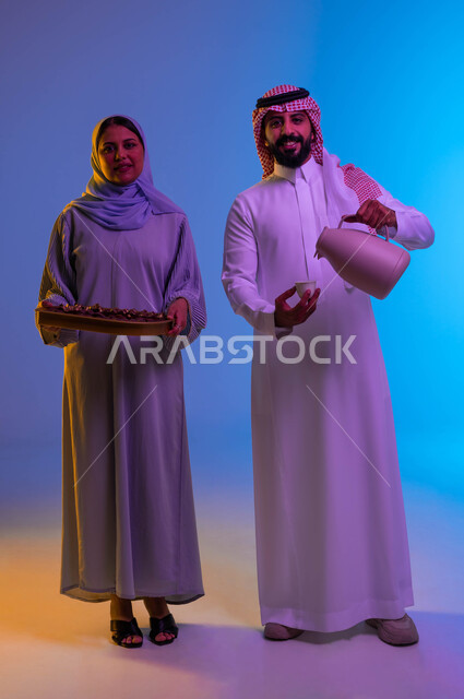 زوجان سعوديان عربيان خليجيان يحملان ضيافة العيد، اجواء العائلة السعودية في العيد، رجل يصب القهوة في الفنجان، امرأة تحمل طبق حلوى العيد، بهجة العيد، عادات العيد في المجتمع السعودي، العيد بين الأهل، الاحتفال بالعيد السعيد، اعياد ومناسبات