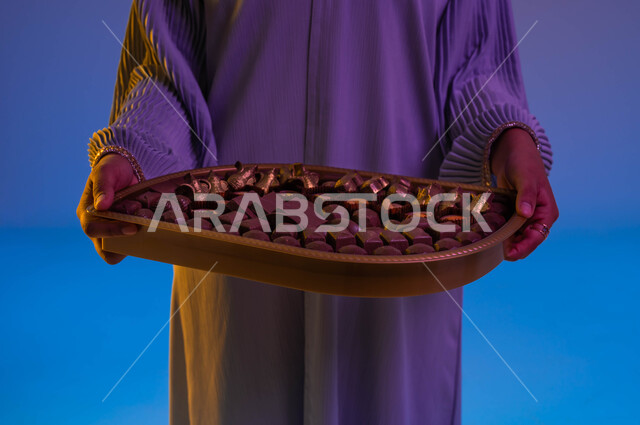 صورة مقربة لامرأة عربية خليجية سعودية تحمل طبق حلوى العيد، ضيافة العيد، بهجة وفرحة العيد، الاحتفال بالعيد السعيد، اعياد ومناسبات