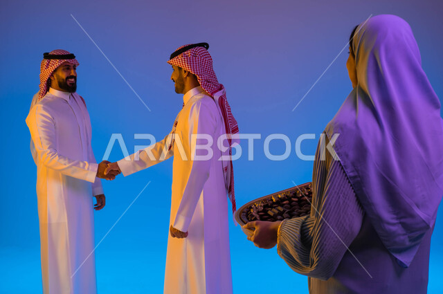A Saudi Arab woman carrying a plate of Eid sweets, Eid hospitality, two Saudi Gulf men shaking hands warmly, Eid visits, the atmosphere of the Saudi family in Eid, the joy of Eid, the atmosphere of Eid, Eid customs in Saudi society, Eid among family, cele