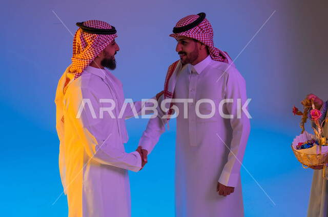 رجلان عربيان خليجيان سعوديان يتصافحان، امرأة تقوم بتقديم ضيافة العيد، اجواء العائلة السعودية في العيد، العيد بين الأهل، اللمة العائلية، عادات العيد في المجتمع السعودي، زيارات العيد، الاحتفال بالعيد السعيد، الحلوى والقرقيعان، أعياد ومناسبات