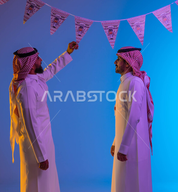 رجلان عربيان خليجيان سعوديان، رجل يمسك زينة العيد، بهجه وفرحة العيد، استقبال العيد، العيد بين الأهل، الاحتفال بالعيد السعيد، أعياد ومناسبات، خلفية ملونة 