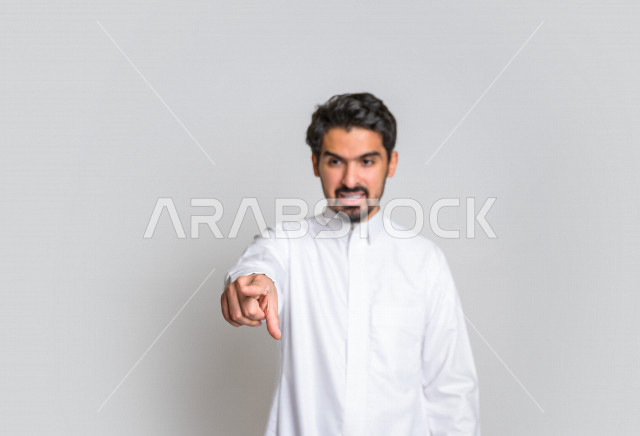 بورتريه لرجل عربي سعودي خليجي باللباس السعودي التقليدي ,  إشارات يدين تدل على العصبية والإشارة الى شخص ما , إيماءات وجه و يدين تدل على الغضب ، الإشارة بإصبع السبابة الى شيء ما , خلفية بيضاء .